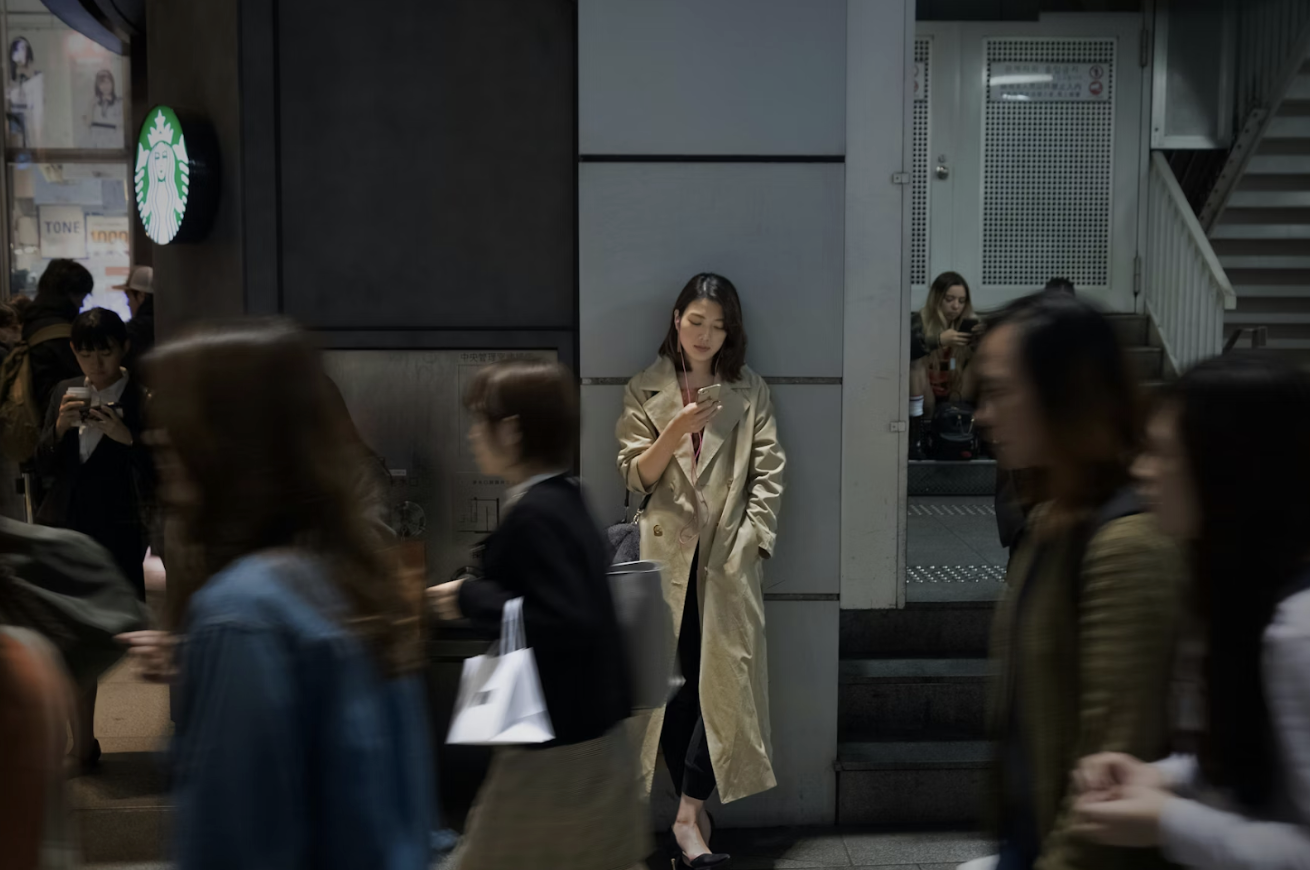 女士穿著卡其色風衣，站在夜間街道邊看手機，象徵都市孤獨與思考